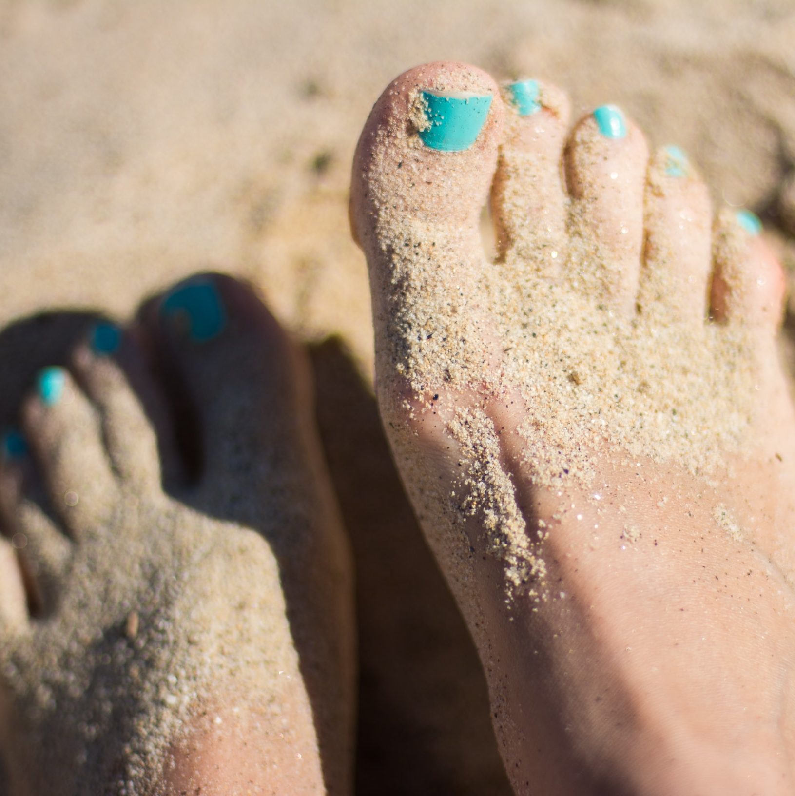 feet in the sand with blue toenails